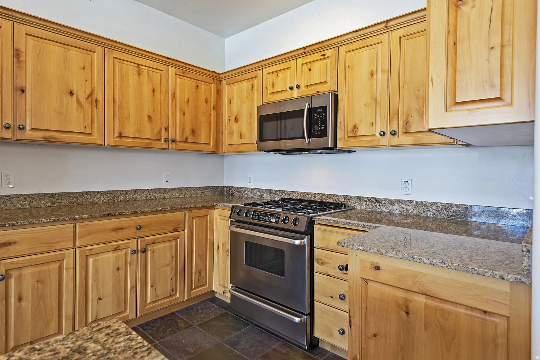 Wood-finish cabinetry with dark hardware, stone countertops, stainless steel range, and stainless steel microwave