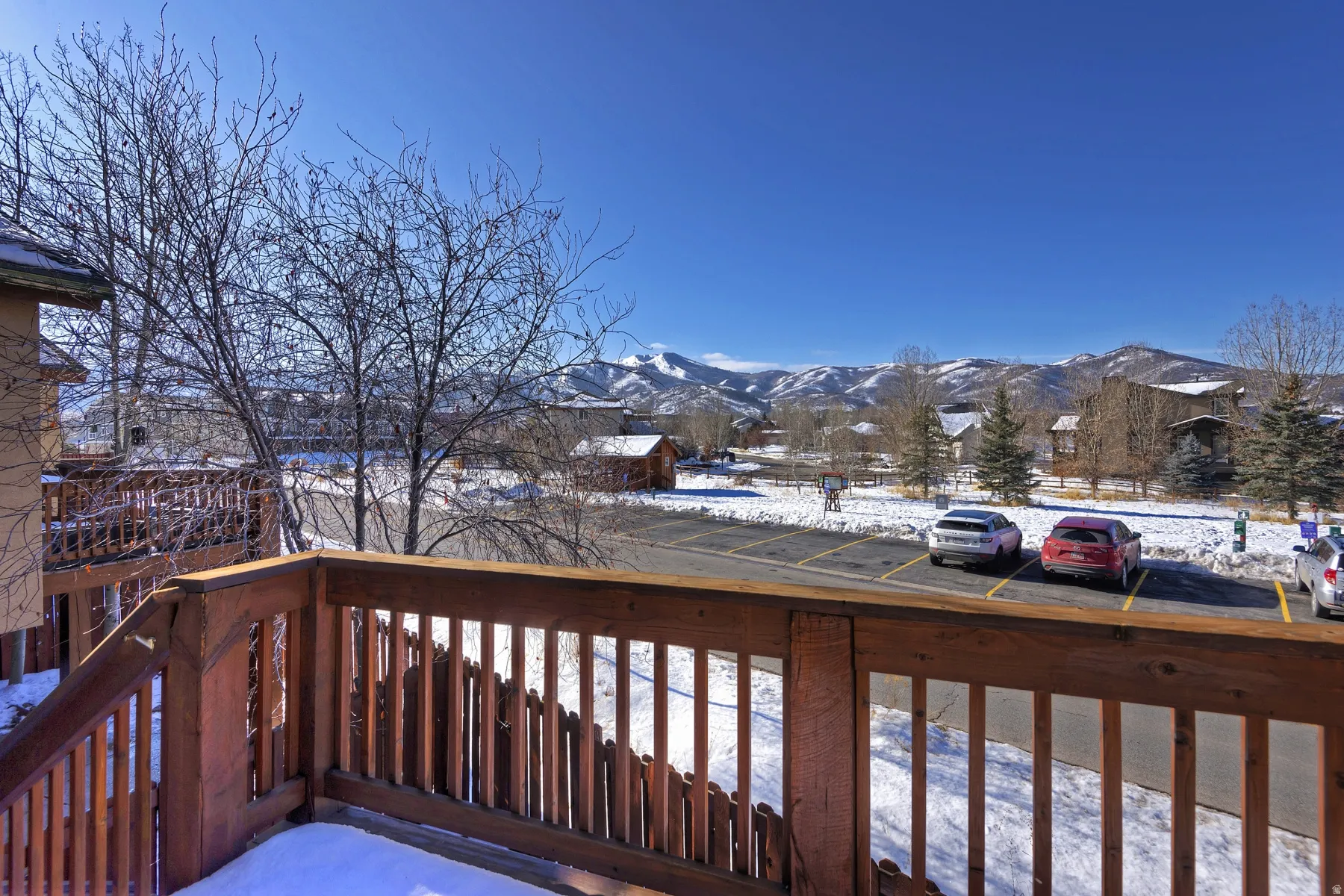 Wood-tone deck railing with a mountain backdrop, mature trees, and a developed area