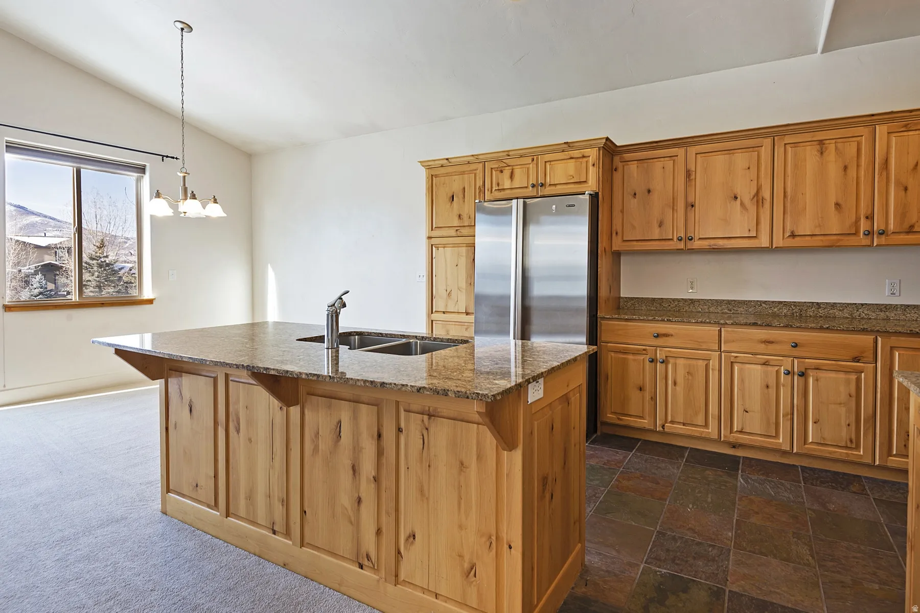Vaulted ceiling, wood cabinetry, granite countertops, stainless steel refrigerator, and dual basin sink