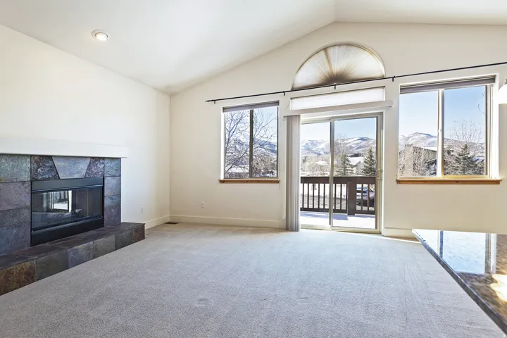 Vaulted ceilings, a slate-tiled fireplace, and a sliding glass door leading to a balcony