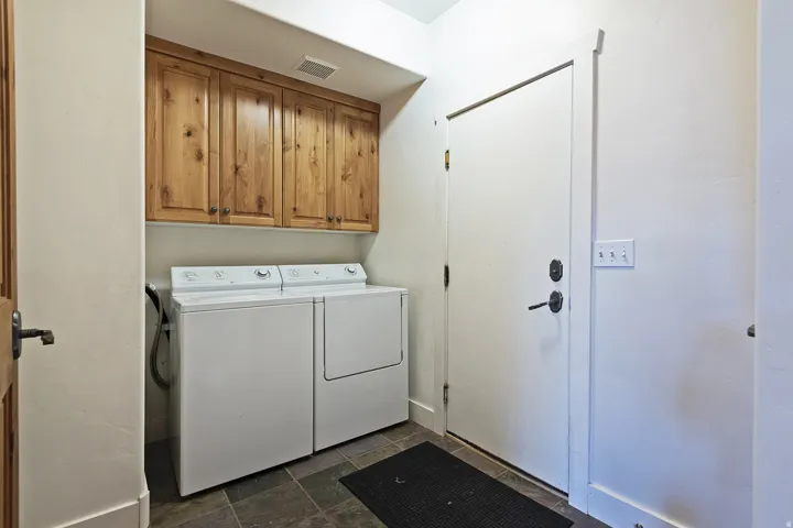 Upper wood cabinetry, tiled flooring, and a solid core door with dark hardware