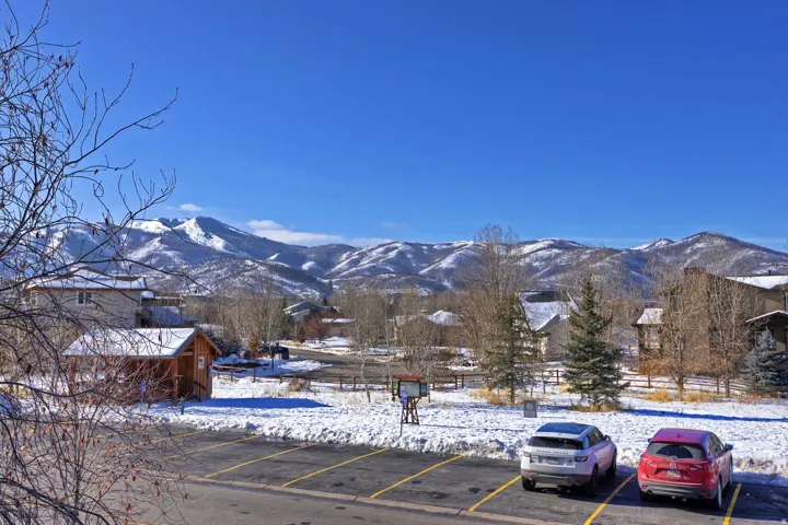 Snow-covered mountains provide a dramatic backdrop to the residential landscape, featuring a paved parking area with yellow striping