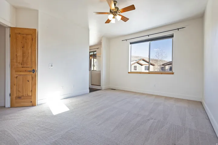 Neutral-toned carpeting, natural wood-finish door, and a ceiling fan with light fixture