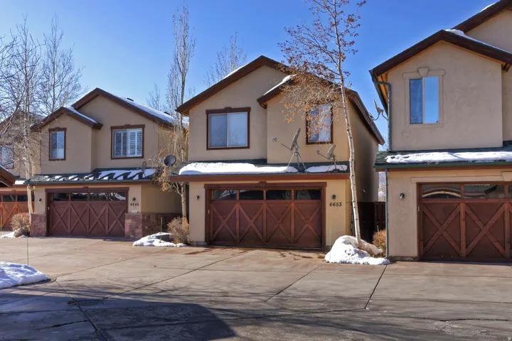 Stucco exterior with gabled roofline, integrated garages featuring wood-finish doors, and stone facade accents