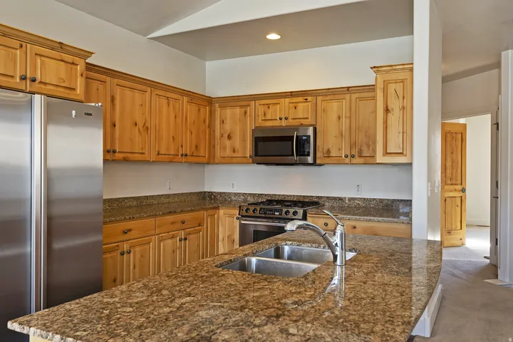 Kitchen featuring light wood cabinetry, stainless steel appliances, a gas range, and granite countertops with an undermount double-basin sink