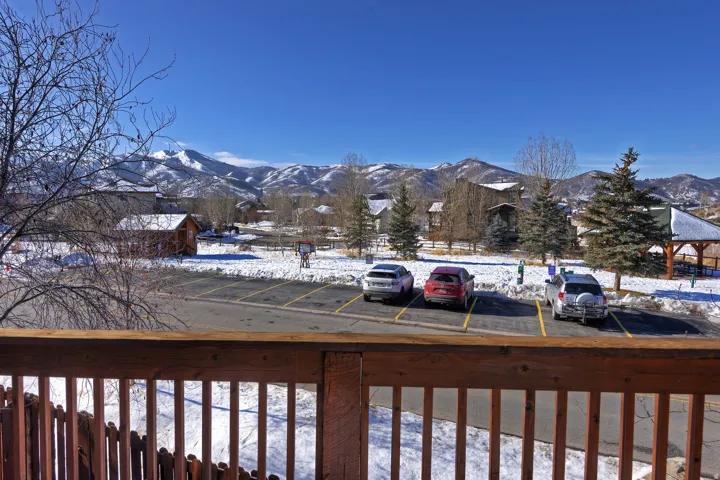Wood-tone railing with a mountain backdrop, complemented by a paved parking area and snow-covered ground