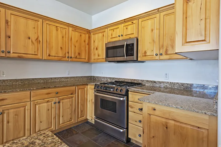 Wood-finish cabinetry with dark hardware, stone countertops, stainless steel range, and stainless steel microwave