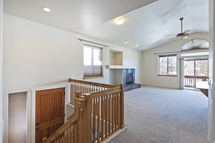 Vaulted ceiling with recessed lighting and ceiling fan, stone-clad fireplace, sliding glass door to exterior, wood railings, and wood door
