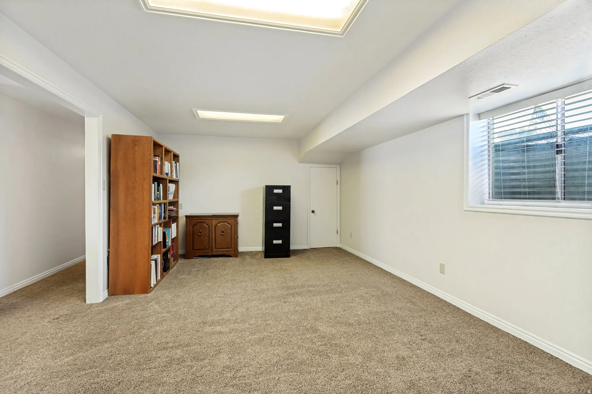 Recessed ceiling lighting, a window with blinds, and neutral carpeting