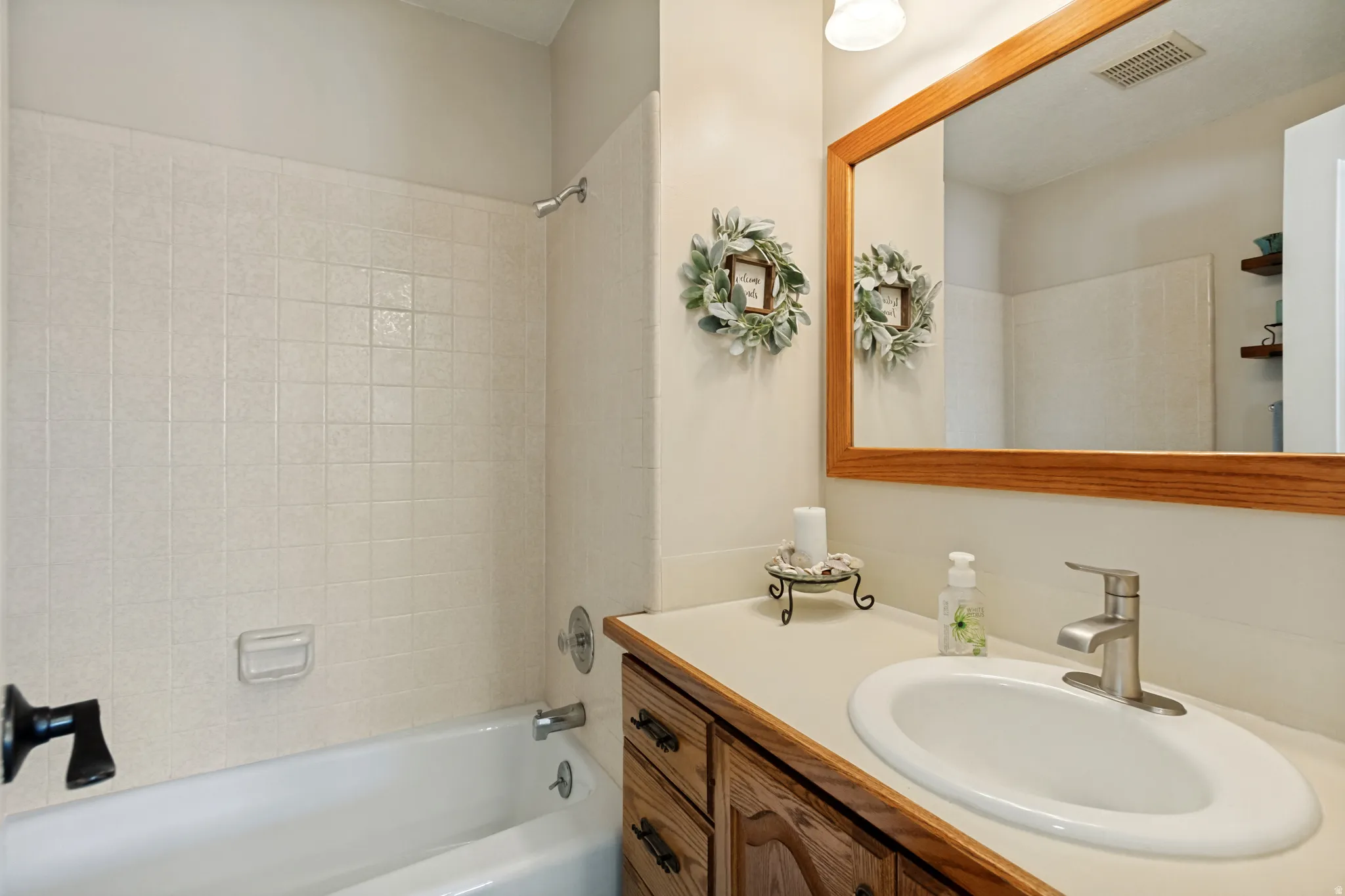 Full bathroom featuring a tub/shower combination with tile surround, a built-in vanity with a laminate countertop, and a wood-framed mirror