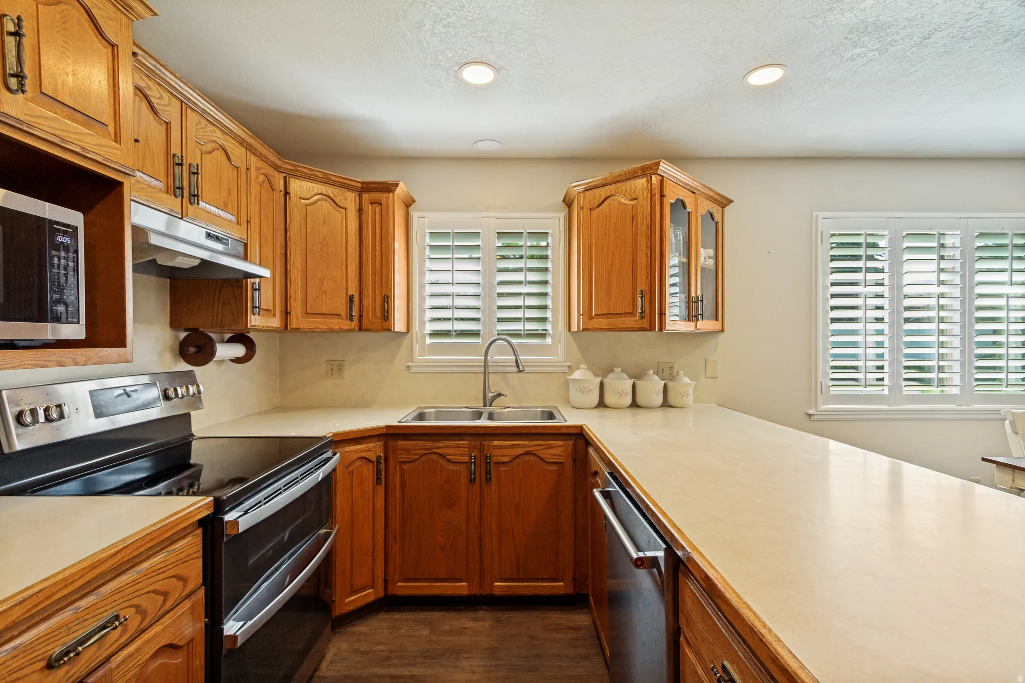 Kitchen featuring wood cabinetry, stainless steel appliances, a double basin sink, ample countertop space, and window shutters