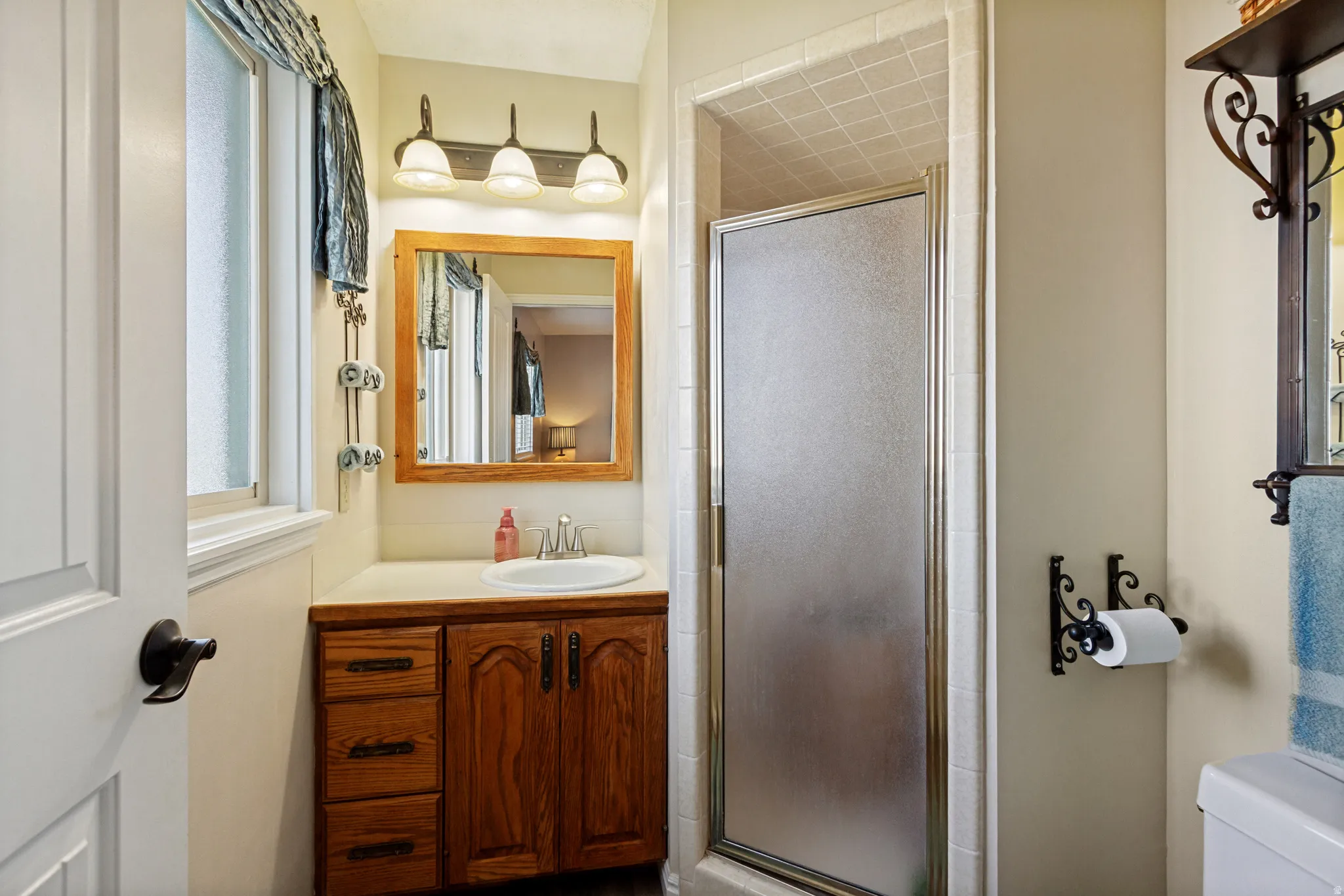 Wood-finish vanity with a white countertop and integrated sink, framed mirror, and a three-light vanity fixture