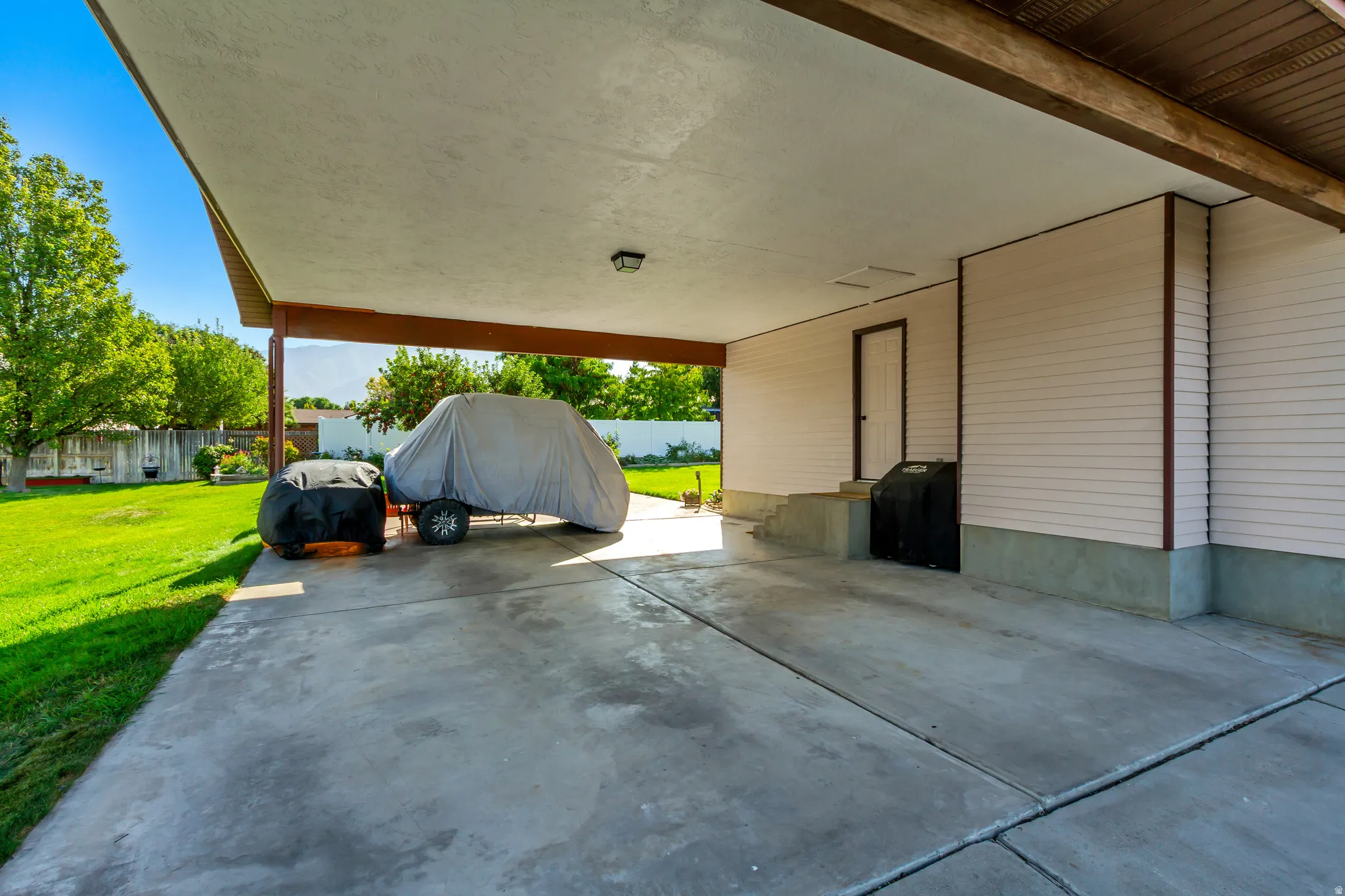 Concrete carport with a stucco ceiling, wood-finish beams, and light-colored siding