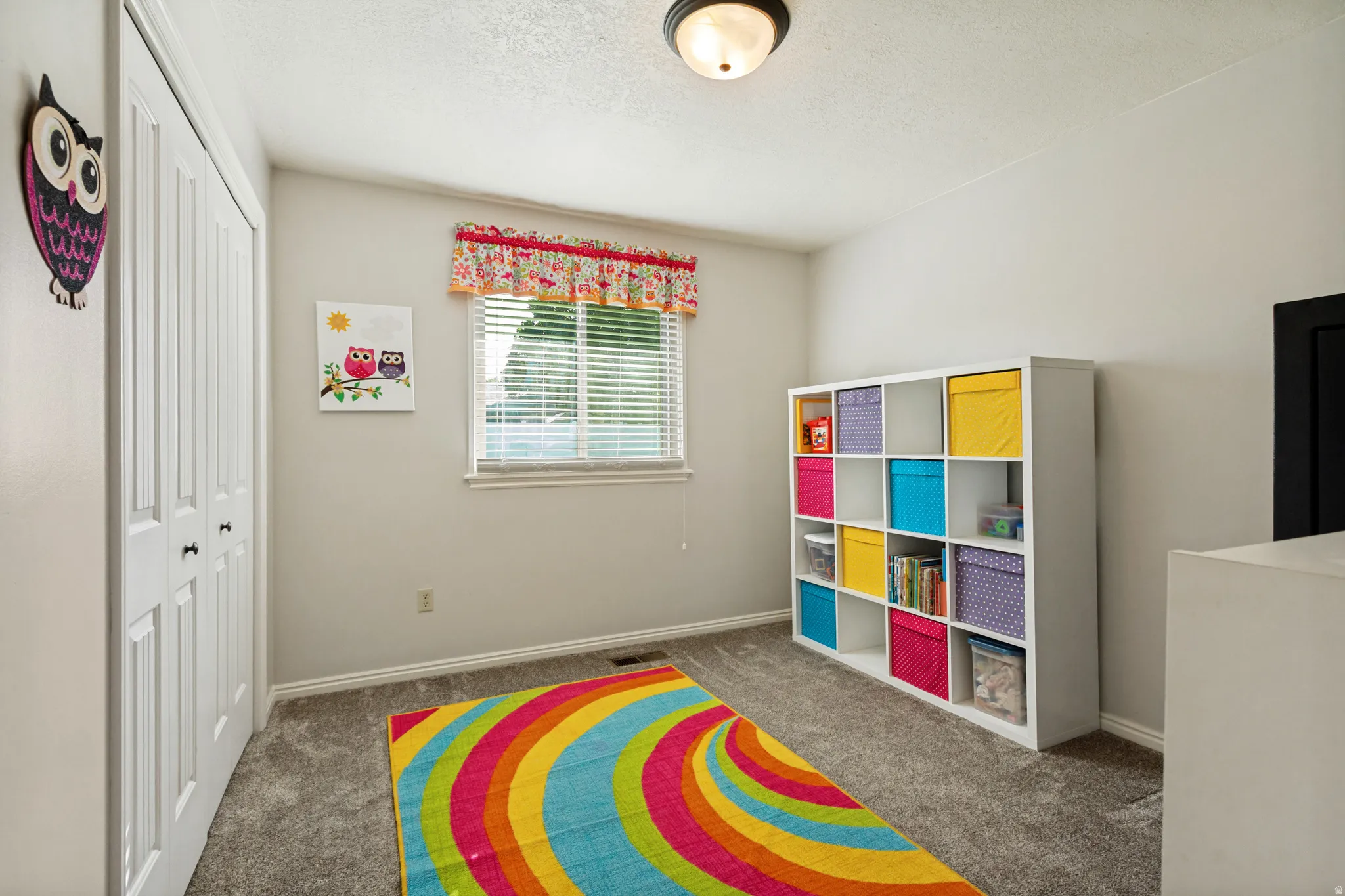 Neutral wall paint, textured ceiling, window with blinds, carpeted flooring, and a flush mount light fixture