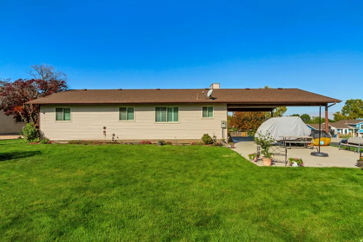 Expansive rear yard featuring a covered patio, concrete hardscaping, and mature landscaping