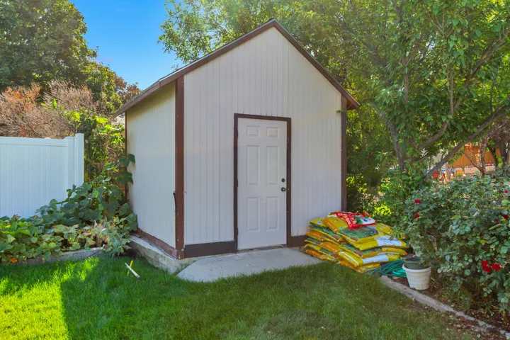 Gable-roof shed featuring vertical siding, a white entry door, and a concrete pad