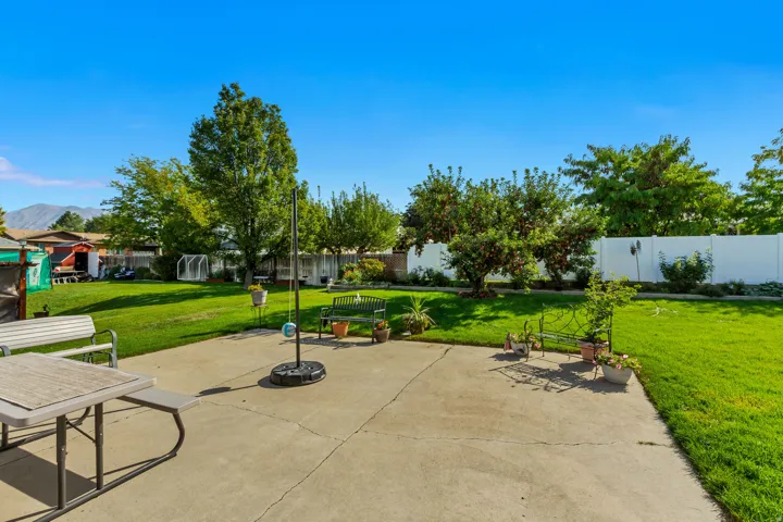 Expansive concrete patio with a lush lawn, mature trees, and a privacy fence