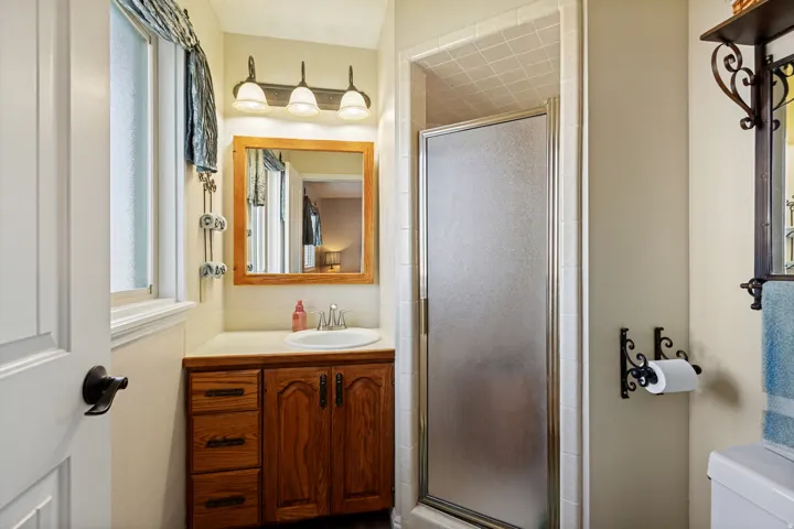 Wood-finish vanity with a white countertop and integrated sink, framed mirror, and a three-light vanity fixture