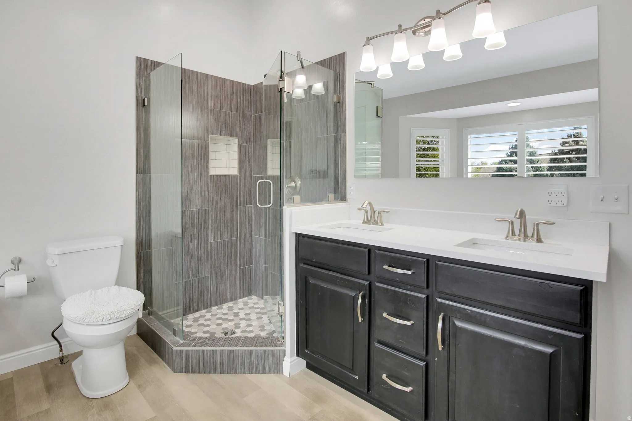 Primary Bath, Recently remodeled. Dual vanity with white countertops and dark cabinetry, glass-enclosed shower with tiled walls and hex-tile flooring, and wood-finish flooring