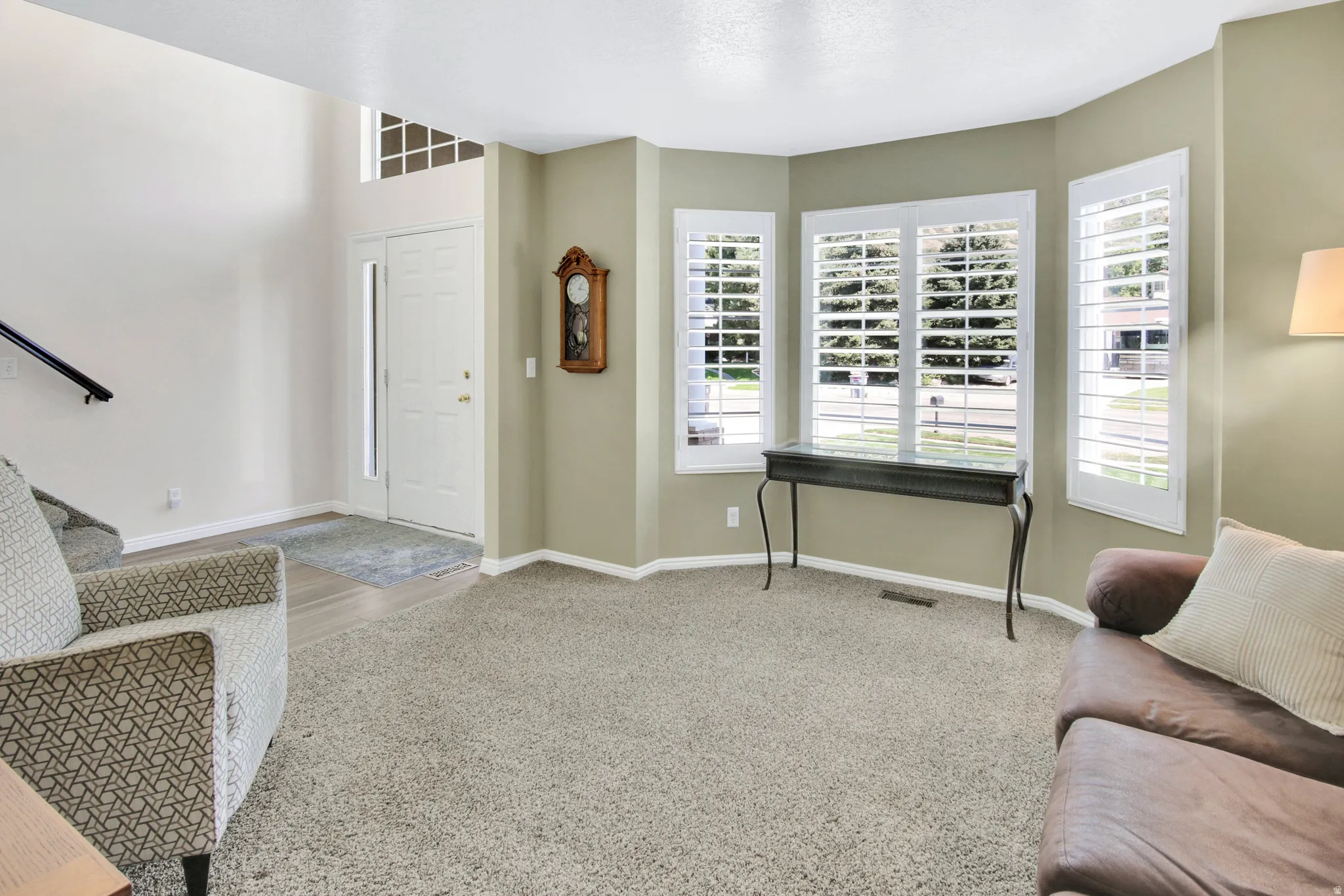 Vaulted entry, carpeted living area, bay windows with plantation shutters, wood-finish flooring at entry, and a white front door with sidelight