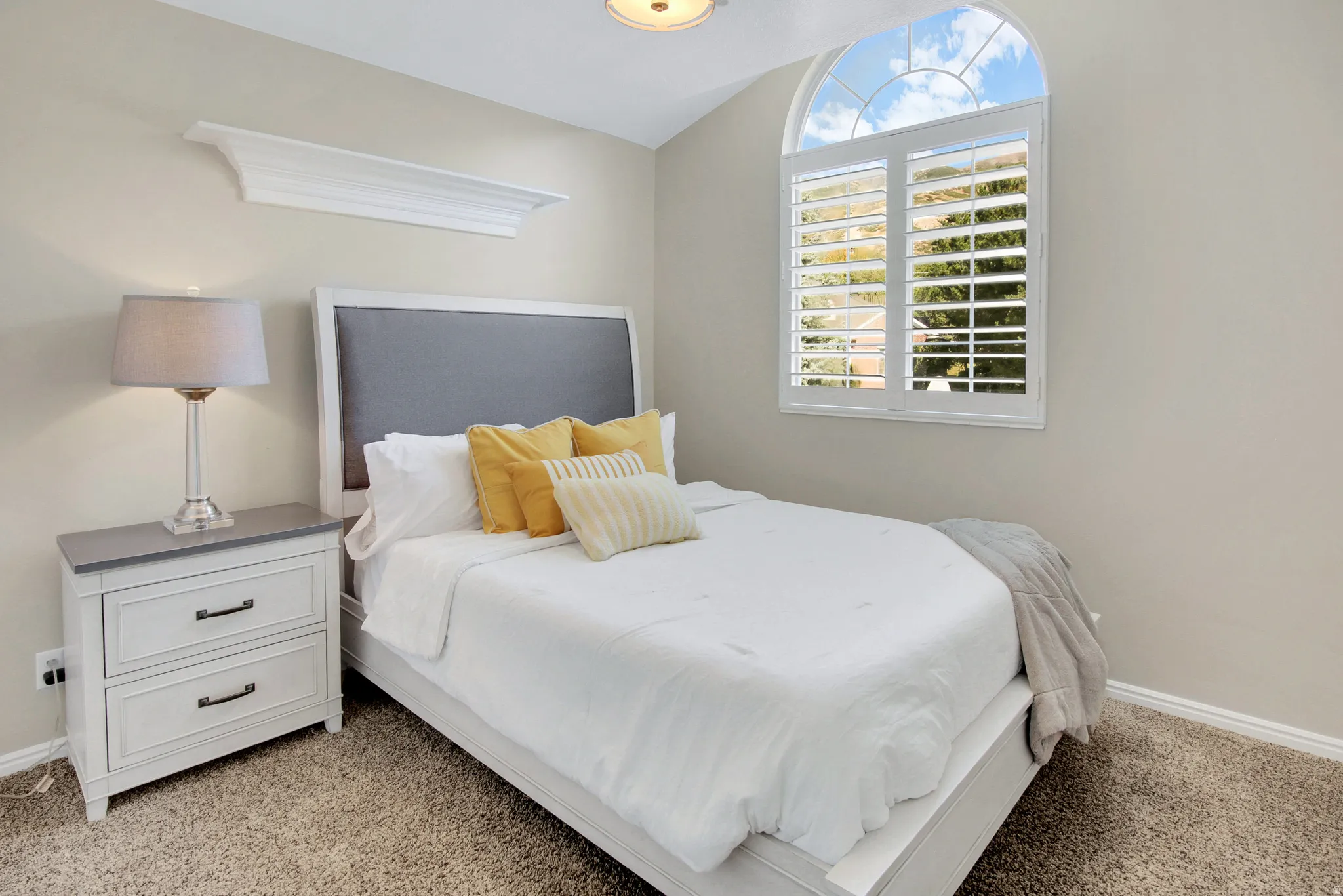 Bedroom #2 Arched window with plantation shutters, vaulted ceiling, built-in wall shelf, and carpeted flooring