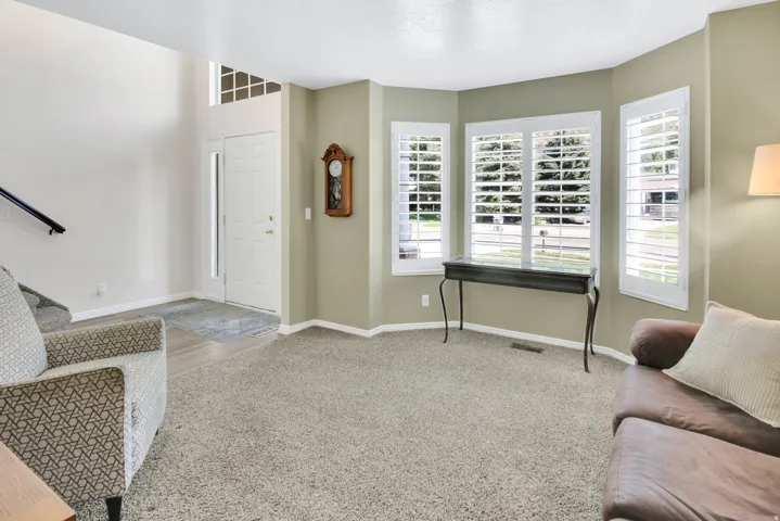 Vaulted entry, carpeted living area, bay windows with plantation shutters, wood-finish flooring at entry, and a white front door with sidelight