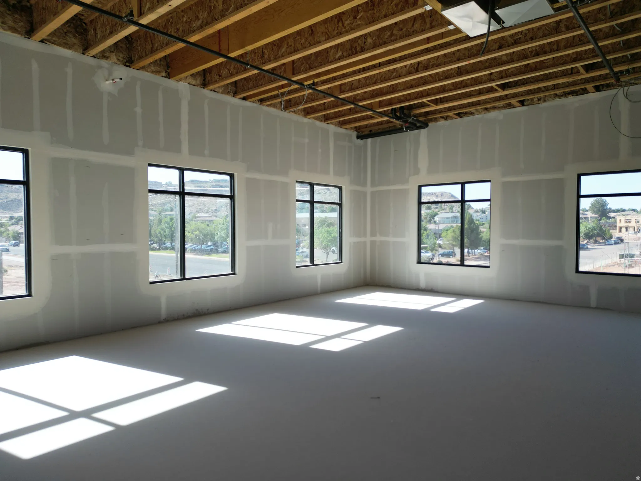 Unfinished interior walls, exposed ceiling joists, multiple windows with black frames, and an unfinished concrete floor
