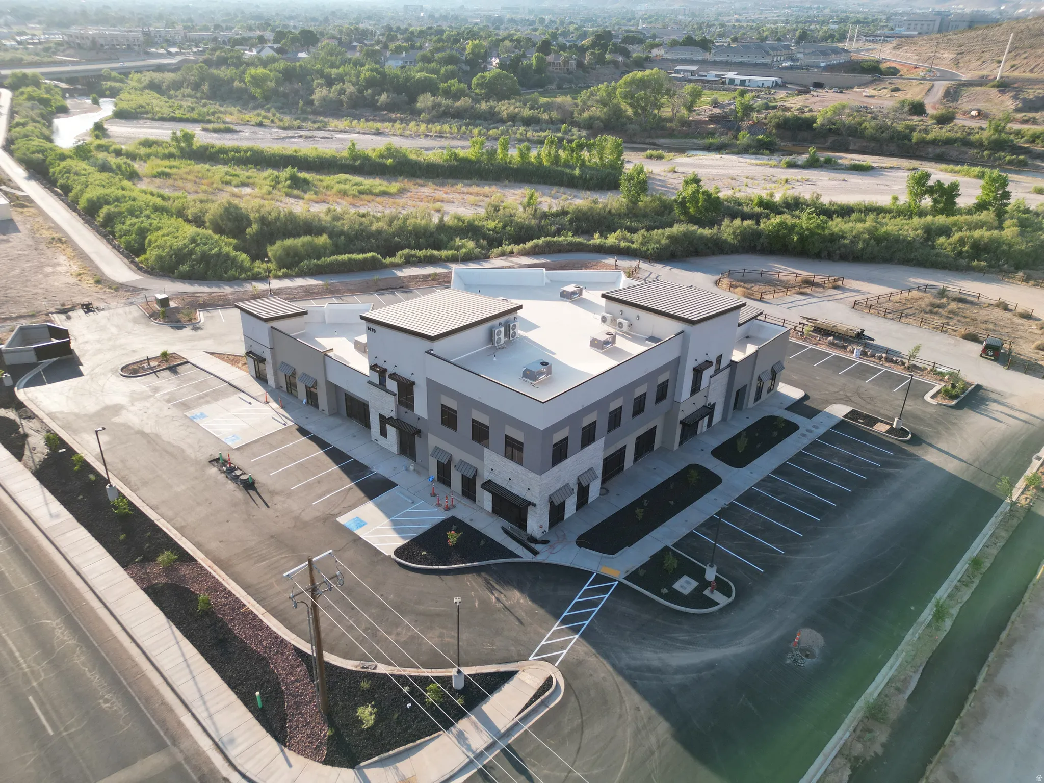 Modern commercial building with a light-toned exterior and dark trim, featuring multiple storefront entrances, a paved parking lot with designated spaces, and landscaped areas