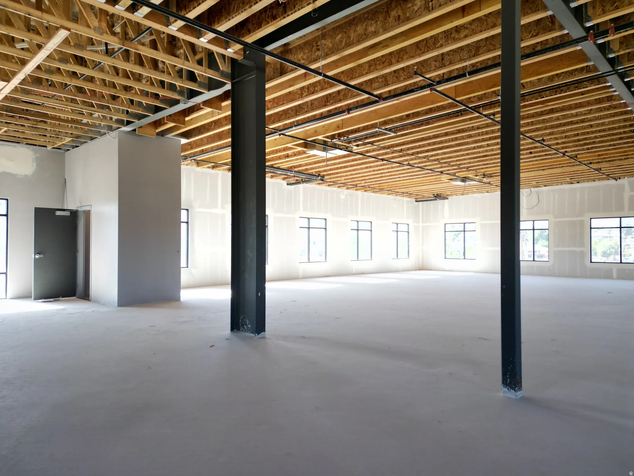 Open-concept commercial space featuring exposed wood beam ceiling, multiple windows, a concrete floor, and structural support columns