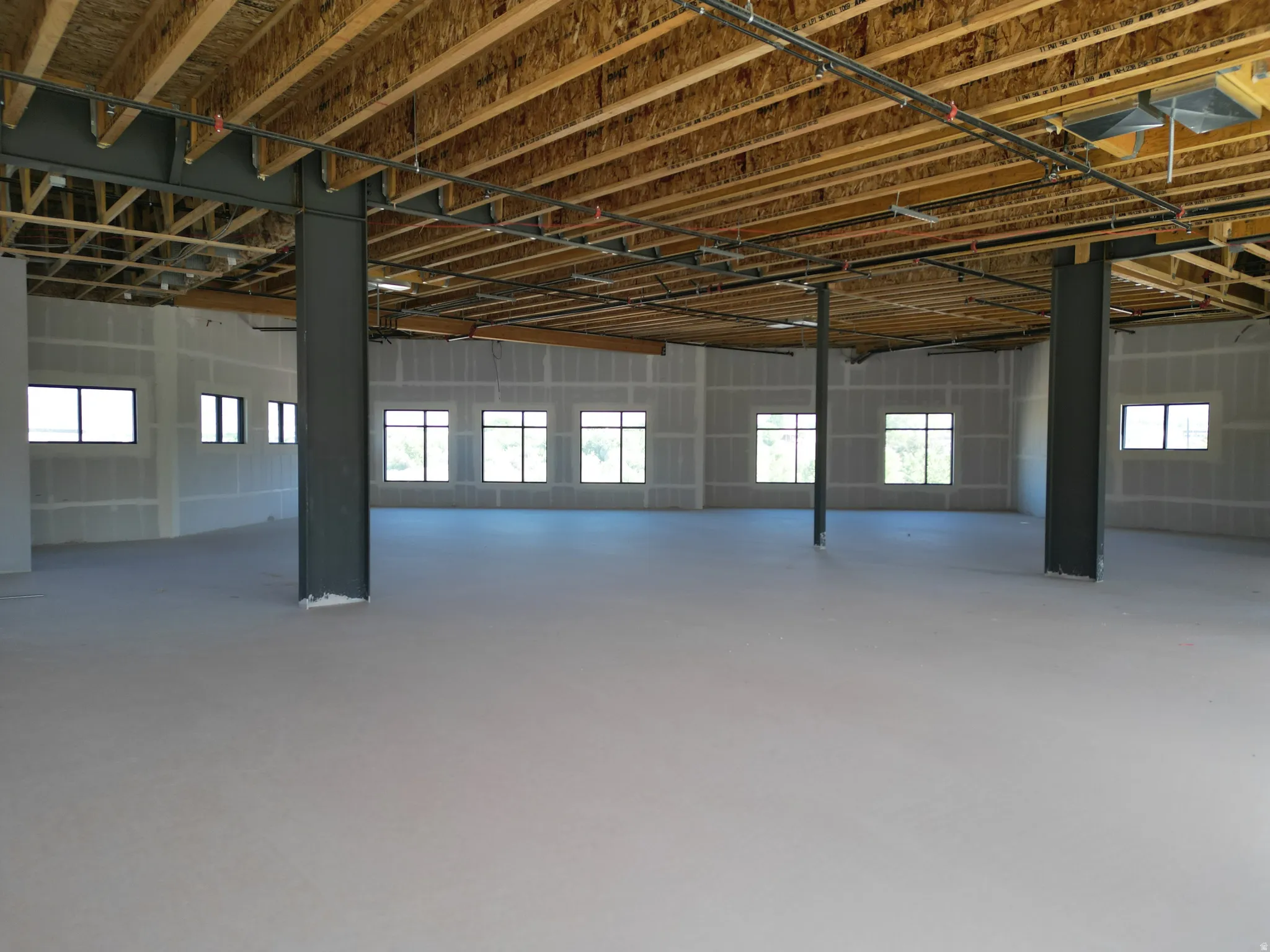 Expansive open-concept space featuring numerous windows, exposed wood ceiling joists, and structural steel columns