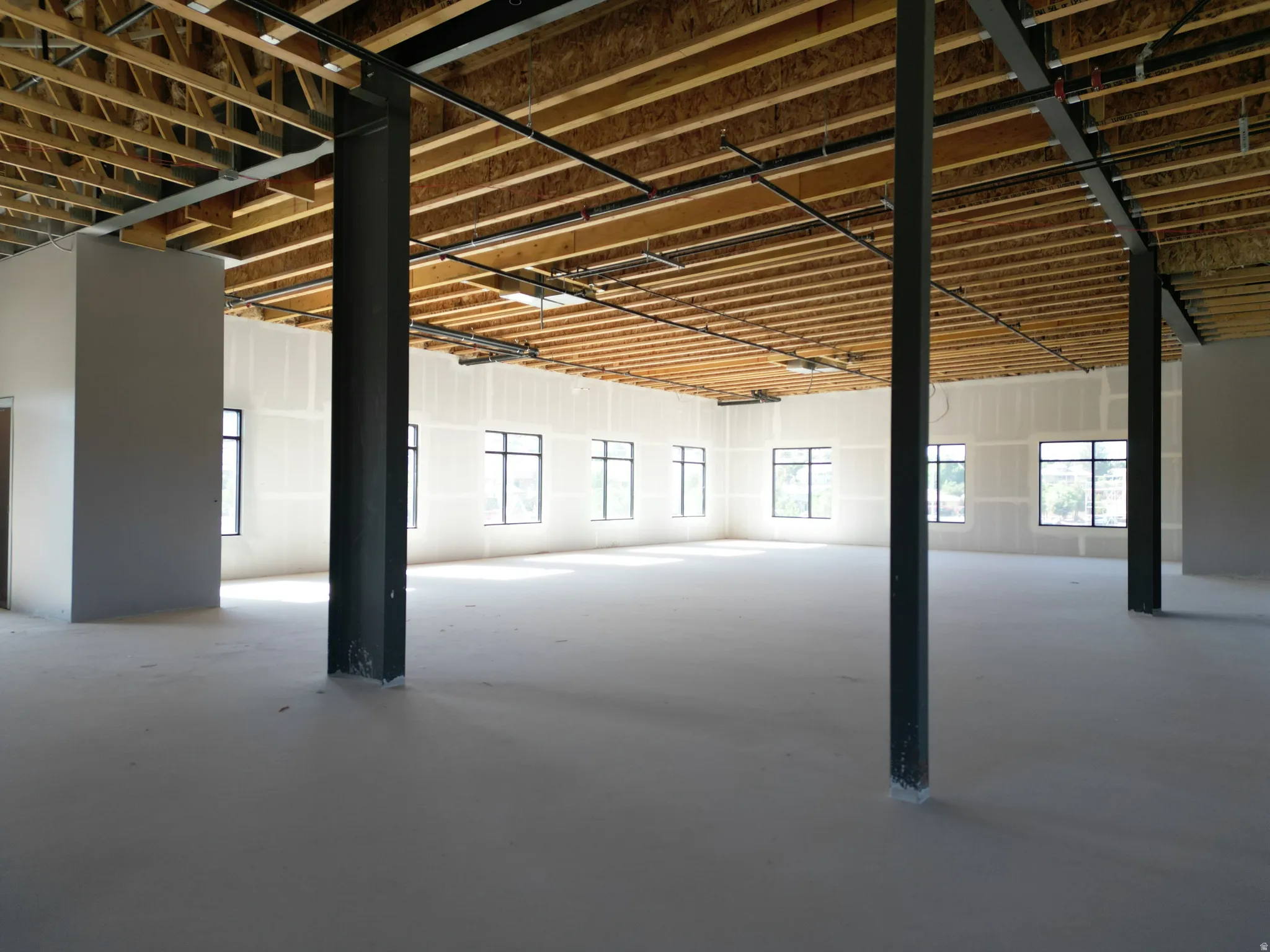 Expansive open-concept space featuring numerous windows, exposed ceiling joists, and structural support beams