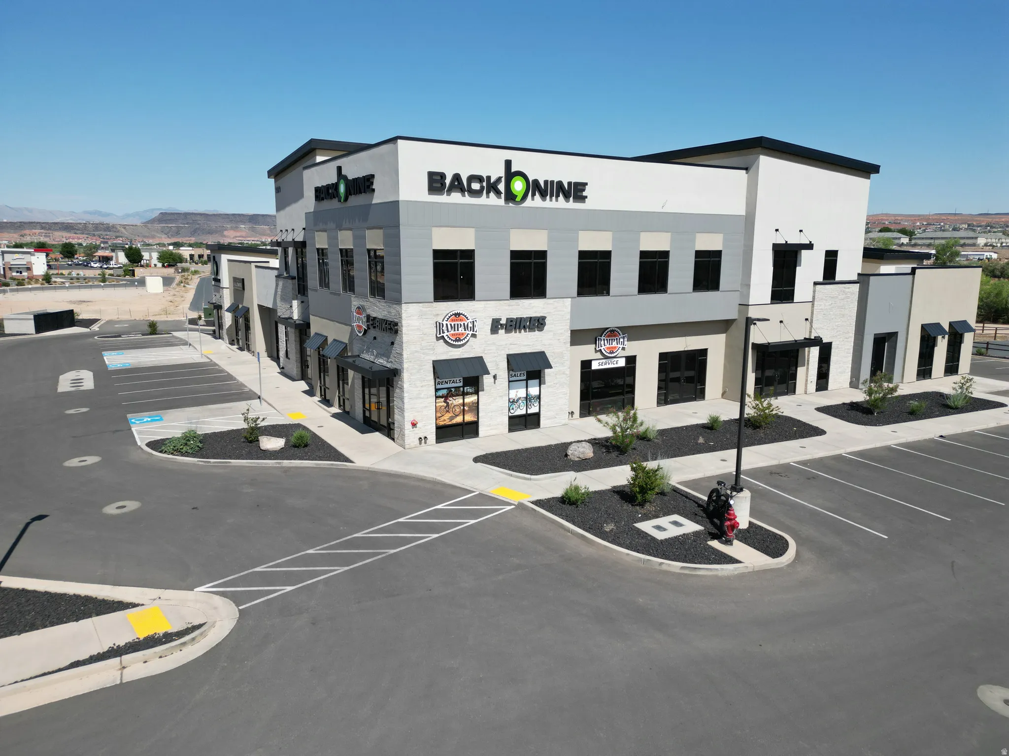 Multi-story building featuring a modern facade with varying materials, numerous storefronts with awnings, and ample paved parking