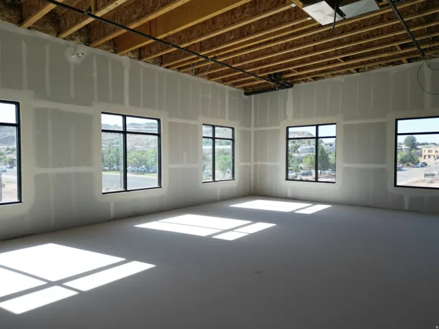 Unfinished interior walls, exposed ceiling joists, multiple windows with black frames, and an unfinished concrete floor