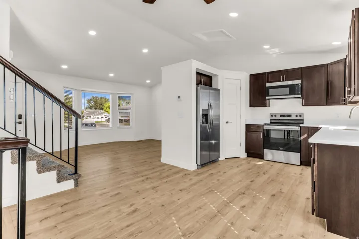 Open-concept living space with wood-finish flooring, recessed lighting, a bay window, and a kitchen featuring stainless steel appliances and dark wood cabinetry