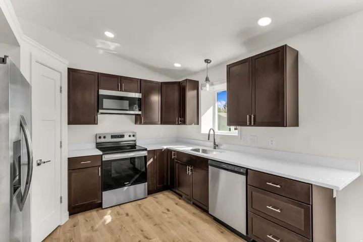 Kitchen featuring stainless steel appliances, dark wood-finish cabinetry, light countertops, wood-finish flooring, and recessed lighting