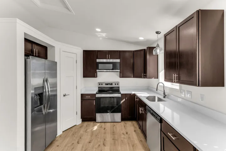 Kitchen featuring wood-finish flooring, dark wood cabinetry, stainless steel appliances, white countertops, and a stainless steel sink with a modern faucet