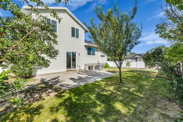 Expansive backyard featuring a manicured lawn, established trees, a concrete patio, and white privacy fencing