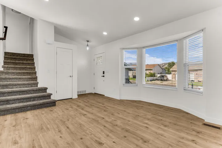 Spacious room featuring wood-finish flooring, a carpeted staircase, a three-panel bay window, recessed lighting, and a front entry door with decorative glass