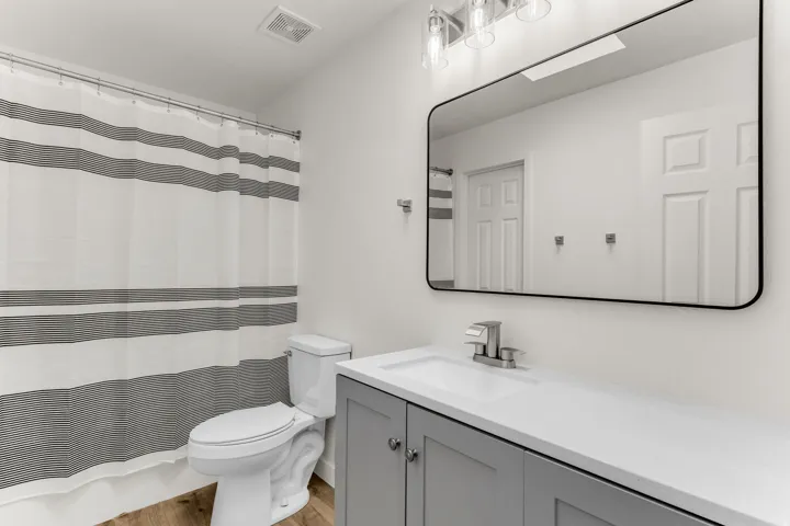 Bathroom featuring a single vanity with gray cabinetry, a white countertop, a rectangular mirror with a black frame, and wood-finish flooring
