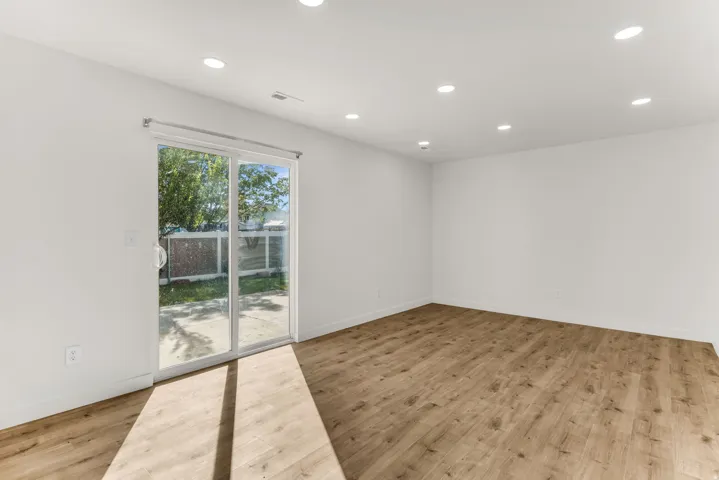 Recessed lighting, wood-finish flooring, sliding glass door, white walls, and outdoor paved area