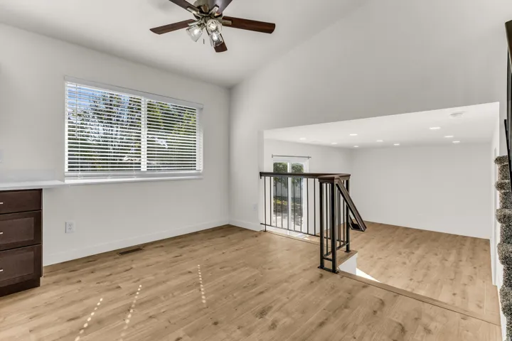 Vaulted ceilings, wood-finish flooring, dark wood cabinetry with light countertop, ceiling fan with integrated lighting, and dark wood railing with metal spindles