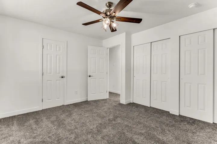 Plush carpet flooring, white interior doors, sliding closet doors, and a ceiling fan with integrated lighting
