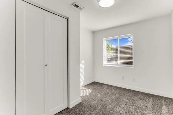 Neutral tone wall paint, carpeted flooring, window with blinds, and white bi-fold closet doors