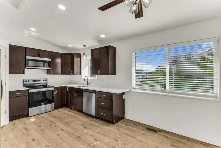 Kitchen featuring dark wood-finish cabinetry, stainless steel appliances, light-toned countertops, wood-finish flooring, and recessed lighting