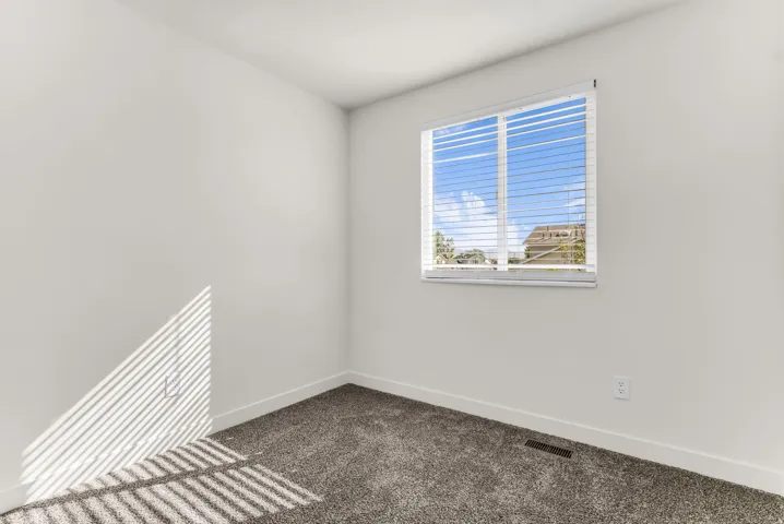 Neutral wall paint, textured carpeting, and a window with horizontal blinds
