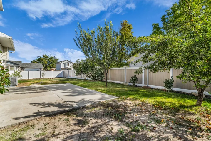 Expansive backyard featuring a concrete patio, mature trees, manicured lawn, and a two-tone privacy fence
