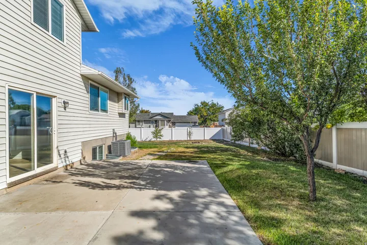 Expansive backyard featuring a concrete patio, a mature tree, a grassy area, and a privacy fence