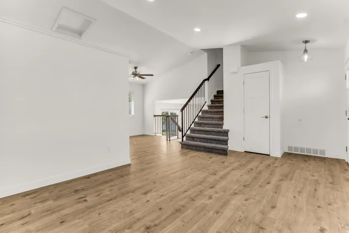 Wood-finish flooring throughout, vaulted ceilings, recessed lighting, ceiling fan, and carpeted staircase with metal balusters