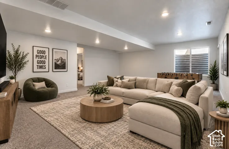 Basement living room. Recessed lighting, light gray carpeting, and a basement window with blinds