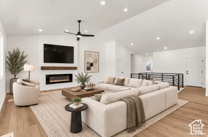 Vaulted ceiling with recessed lighting, engineered wood-finish flooring, built-in electric fireplace with wood mantel, black metal railing, and a ceiling fan